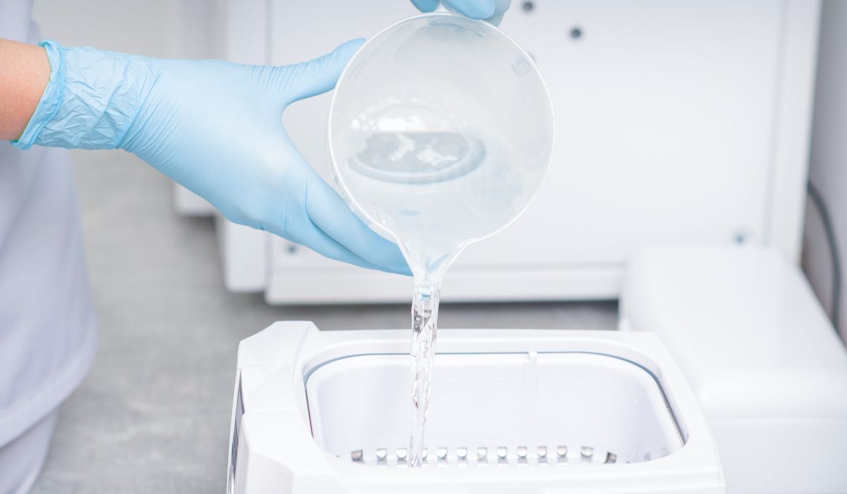 Manos vertiendo agua en máquina autoclave